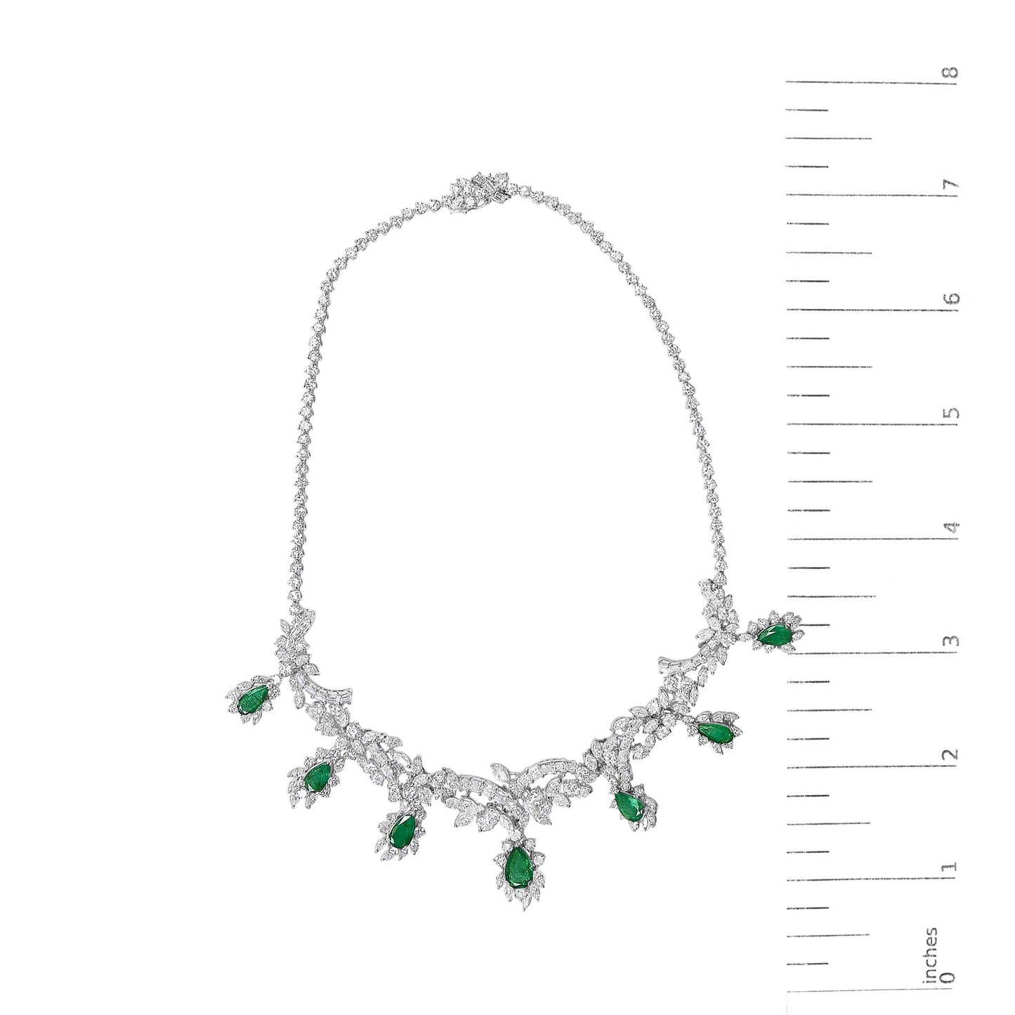 White metal necklace set shown on a scale, featuring a chain with clusters of white gemstones and pear-shaped green gemstones arranged along the lower half. The image is taken from a top-down angle.