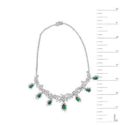 White metal necklace set shown on a scale, featuring a chain with clusters of white gemstones and pear-shaped green gemstones arranged along the lower half. The image is taken from a top-down angle.