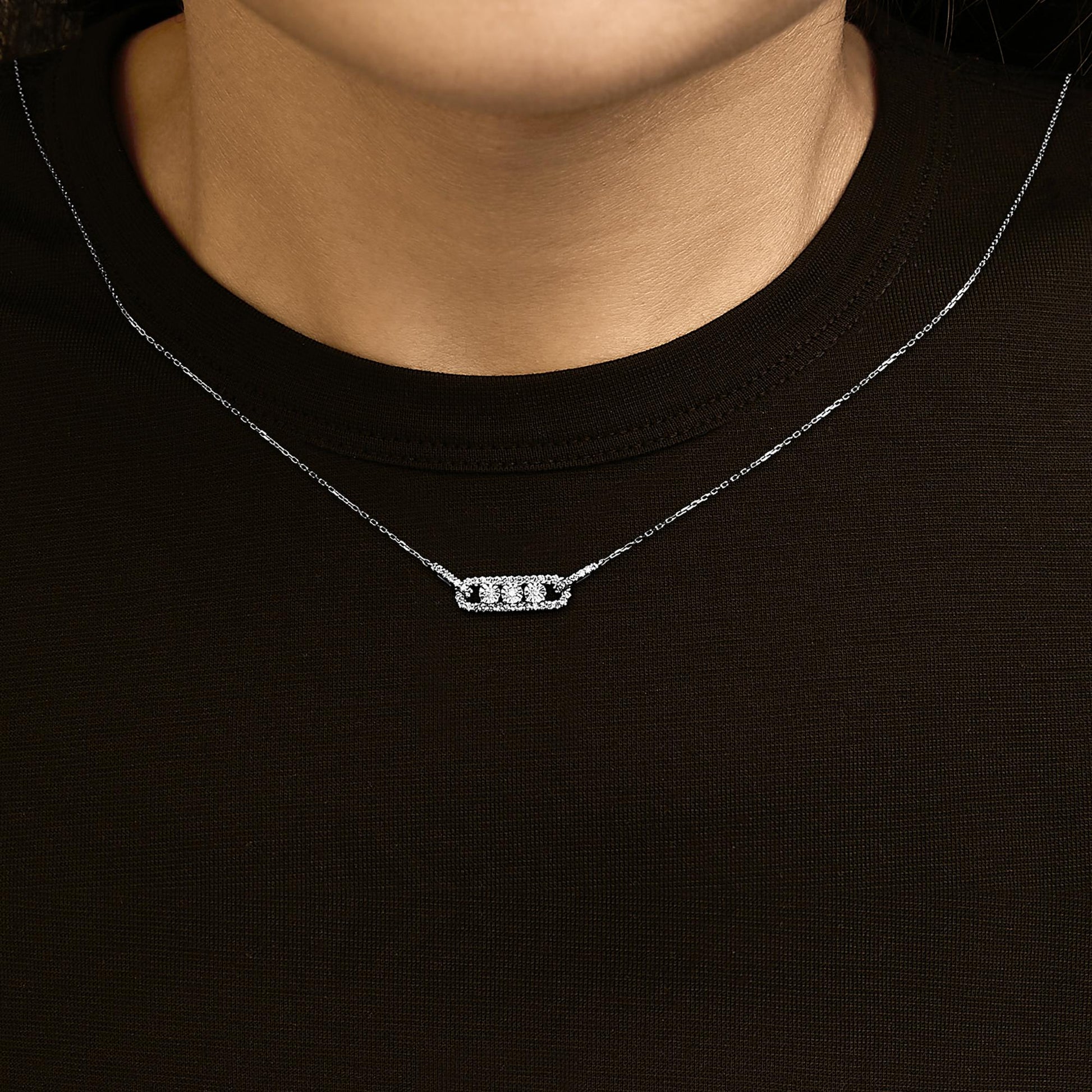 White metal necklace with a horizontal rectangular pendant featuring three round white gemstones in a miracle setting, surrounded by smaller round white gemstones in prong settings, shown worn on a model from the front angle.