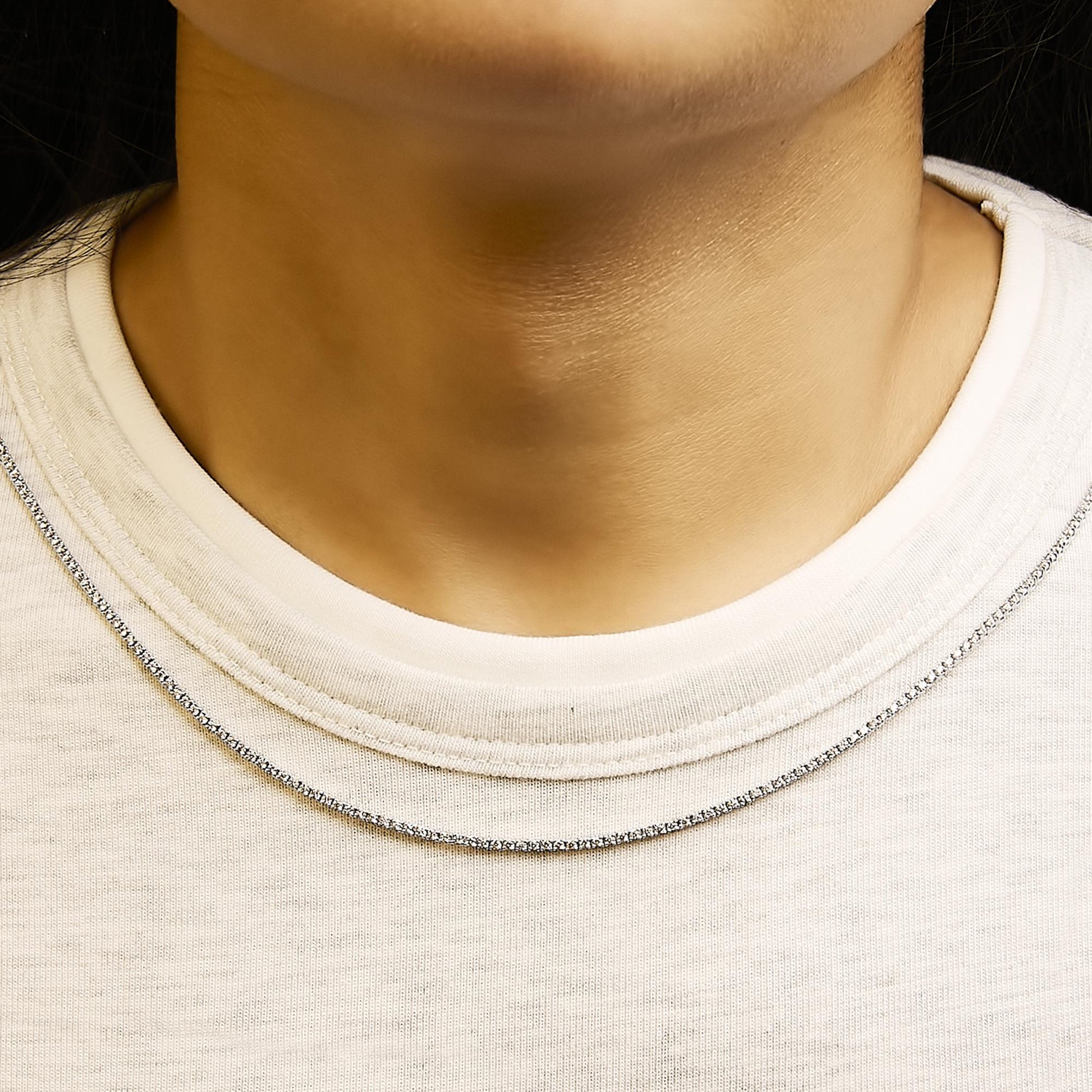 Close-up front view of a model wearing a white metal necklace featuring a thin chain adorned with small round white gemstones in prong settings.