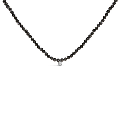 Close-up front view of a white necklace with round black gemstones forming the chain and a single round white gemstone pendant in the center.