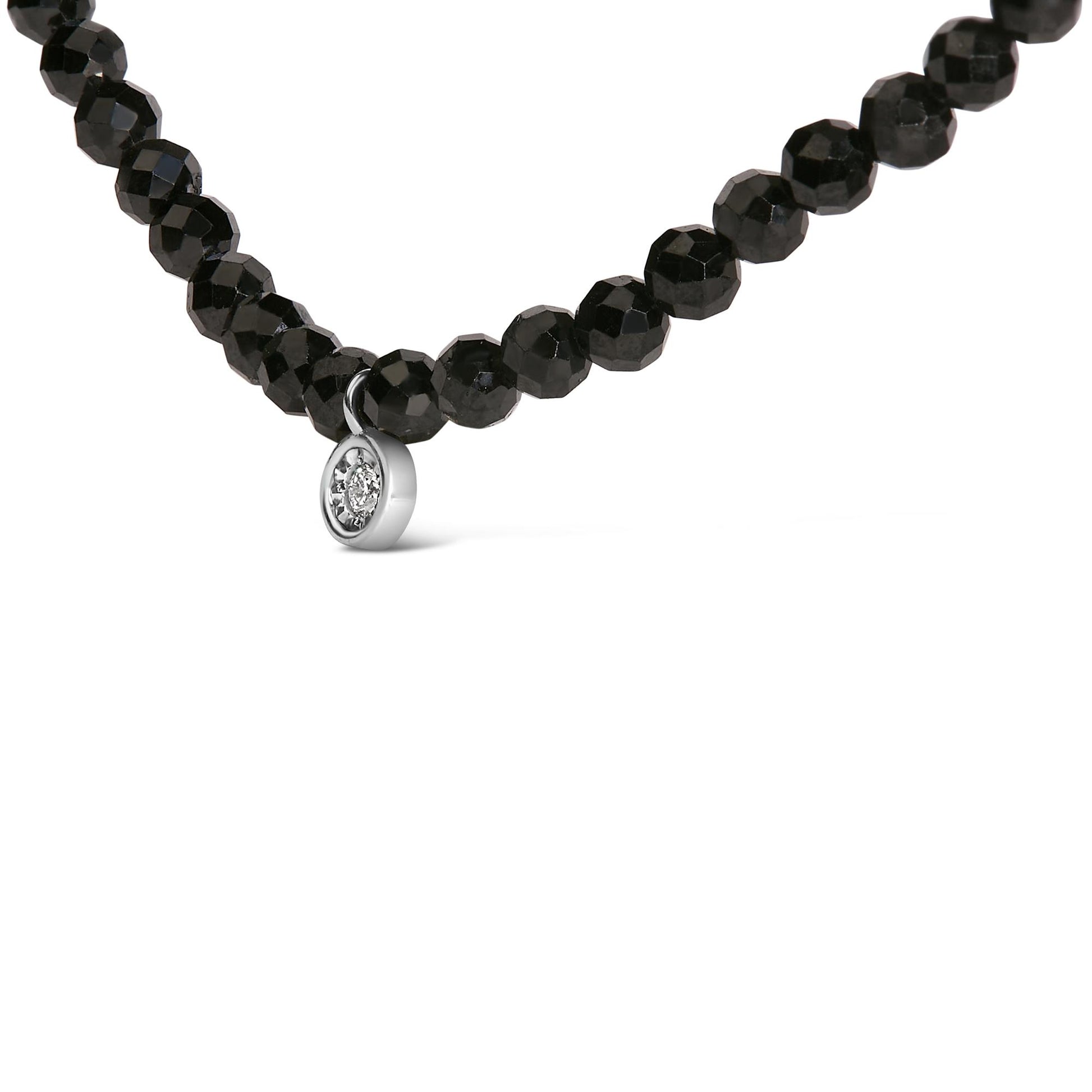 Close-up front angle of a white necklace featuring round black gemstones with a small round white gemstone pendant in a miracle setting.