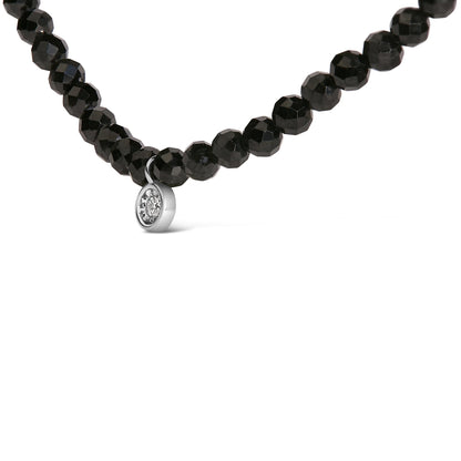 Close-up front angle of a white necklace featuring round black gemstones with a small round white gemstone pendant in a miracle setting.