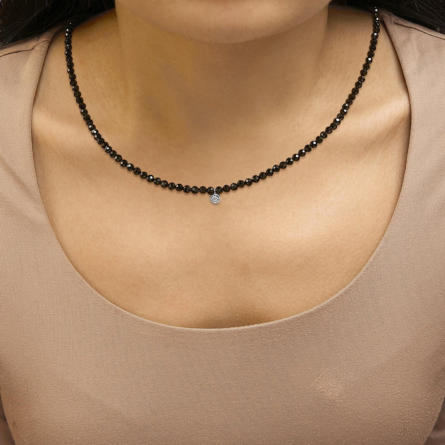 Necklace with round black gemstones and a small white gemstone pendant, shown worn on a model, front close-up view.