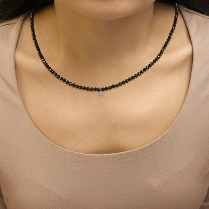 Necklace with round black gemstones and a small white gemstone pendant, shown worn on a model, front close-up view.