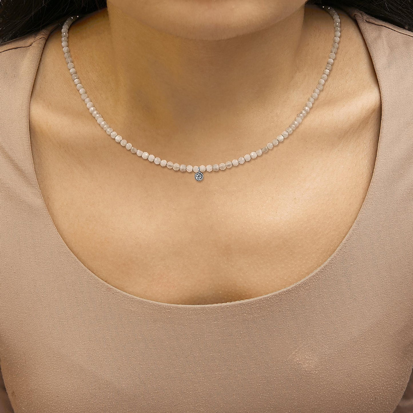 Close-up front view of a white necklace with small round white gemstones and a single round white gemstone pendant, shown worn on a model.