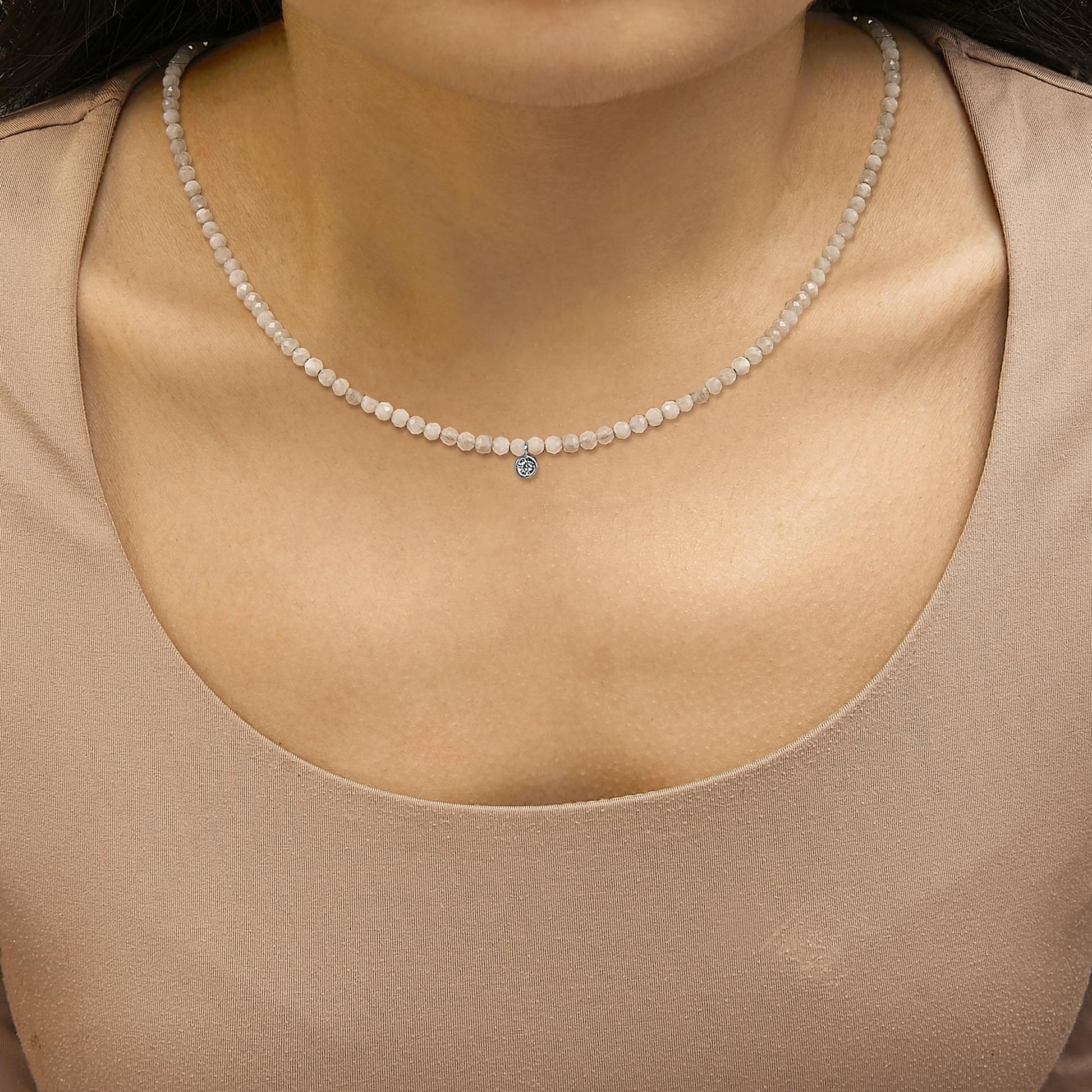 Close-up front view of a white necklace with small round white gemstones and a single round white gemstone pendant, shown worn on a model.