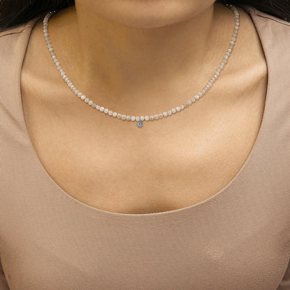 Close-up front view of a white necklace with small round white gemstones and a single round white gemstone pendant, shown worn on a model.