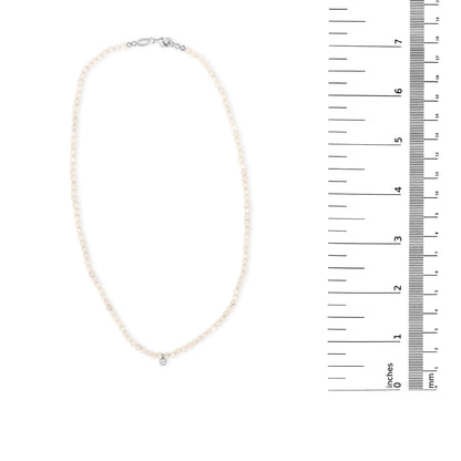 White gemstone beaded necklace with a single white round gemstone pendant shown on a scale, top-down angle.
