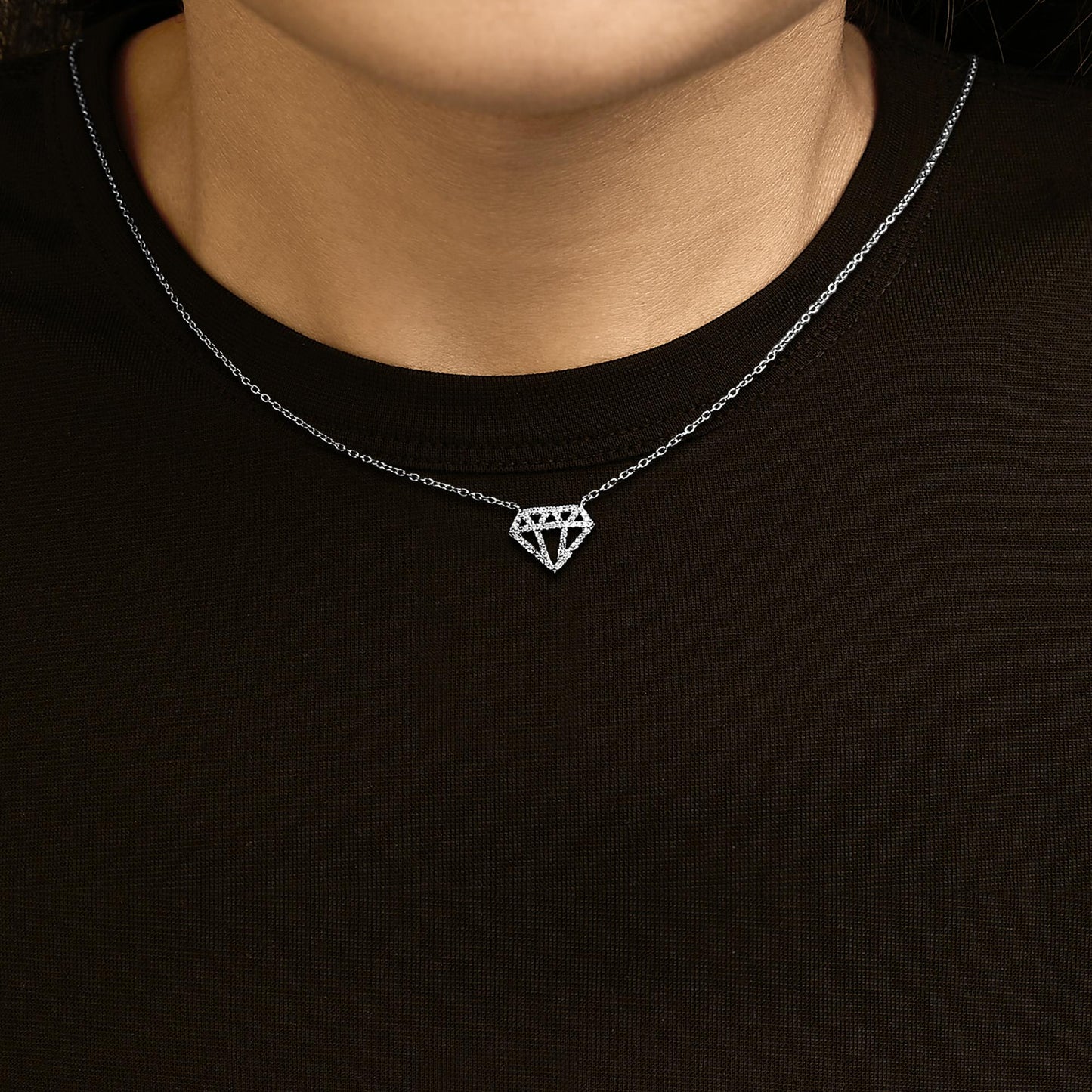 White metal necklace with a diamond-shaped pendant featuring round white gemstones in prong settings, shown worn on a model from the front angle.