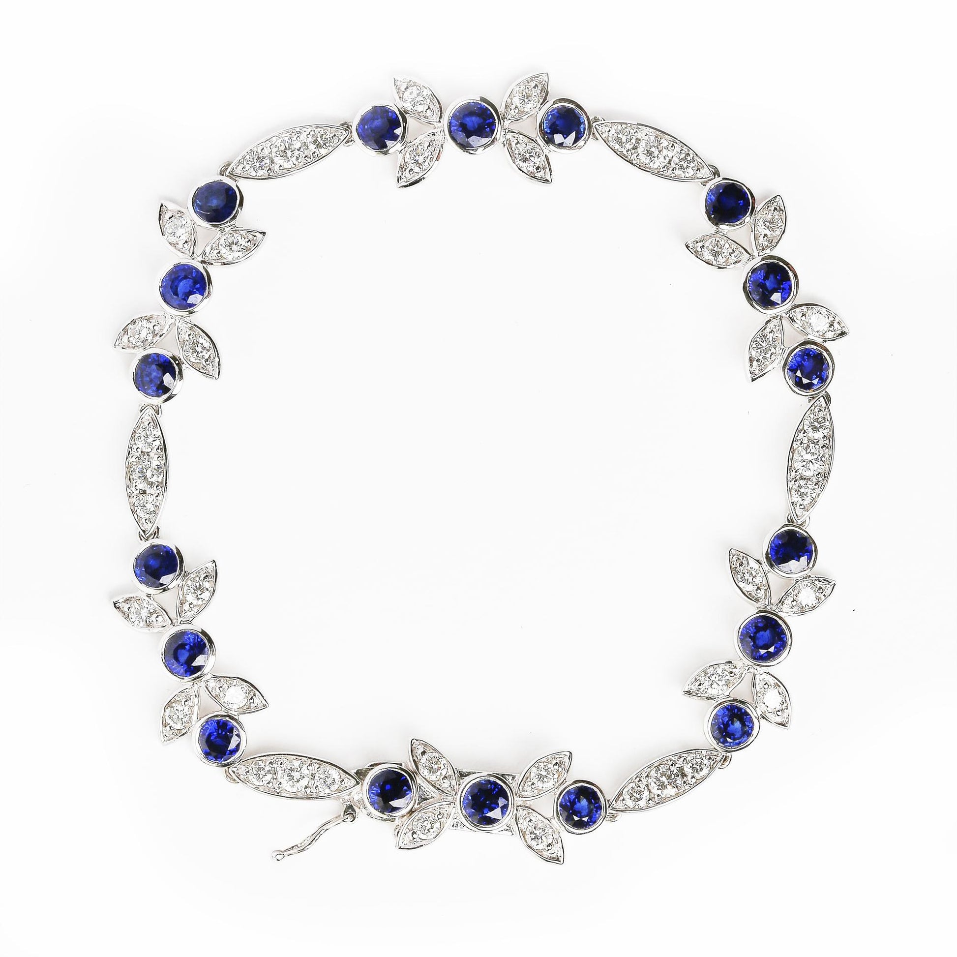 Top-down view of a white metal bracelet with round blue gemstones in bezel settings and round white gemstones in prong settings arranged in leaf and marquise shapes.
