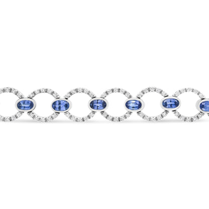Straight-on view of a white metal bracelet featuring alternating circular links set with round white gemstones and oval blue gemstones in bezel settings.