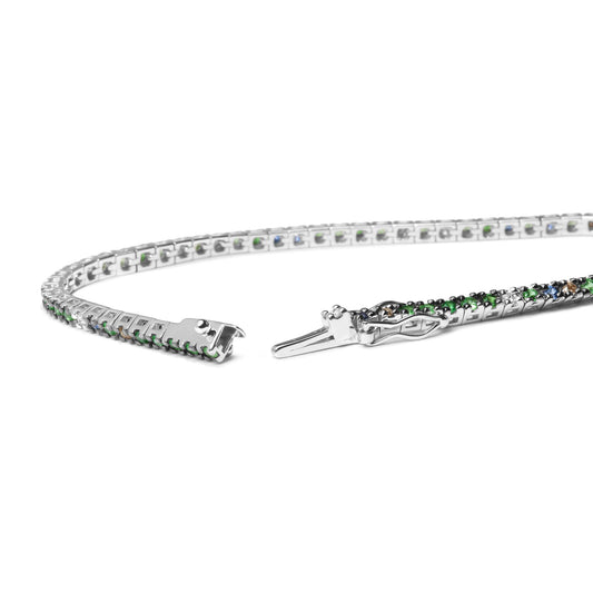 Close-up image of an open white metal bracelet laid flat, featuring prong-set round white, brown, blue, and green gemstones, shot from an angled side view.