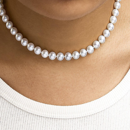 Close-up front view of a white pearl necklace worn on a model's neck above a white ribbed top.