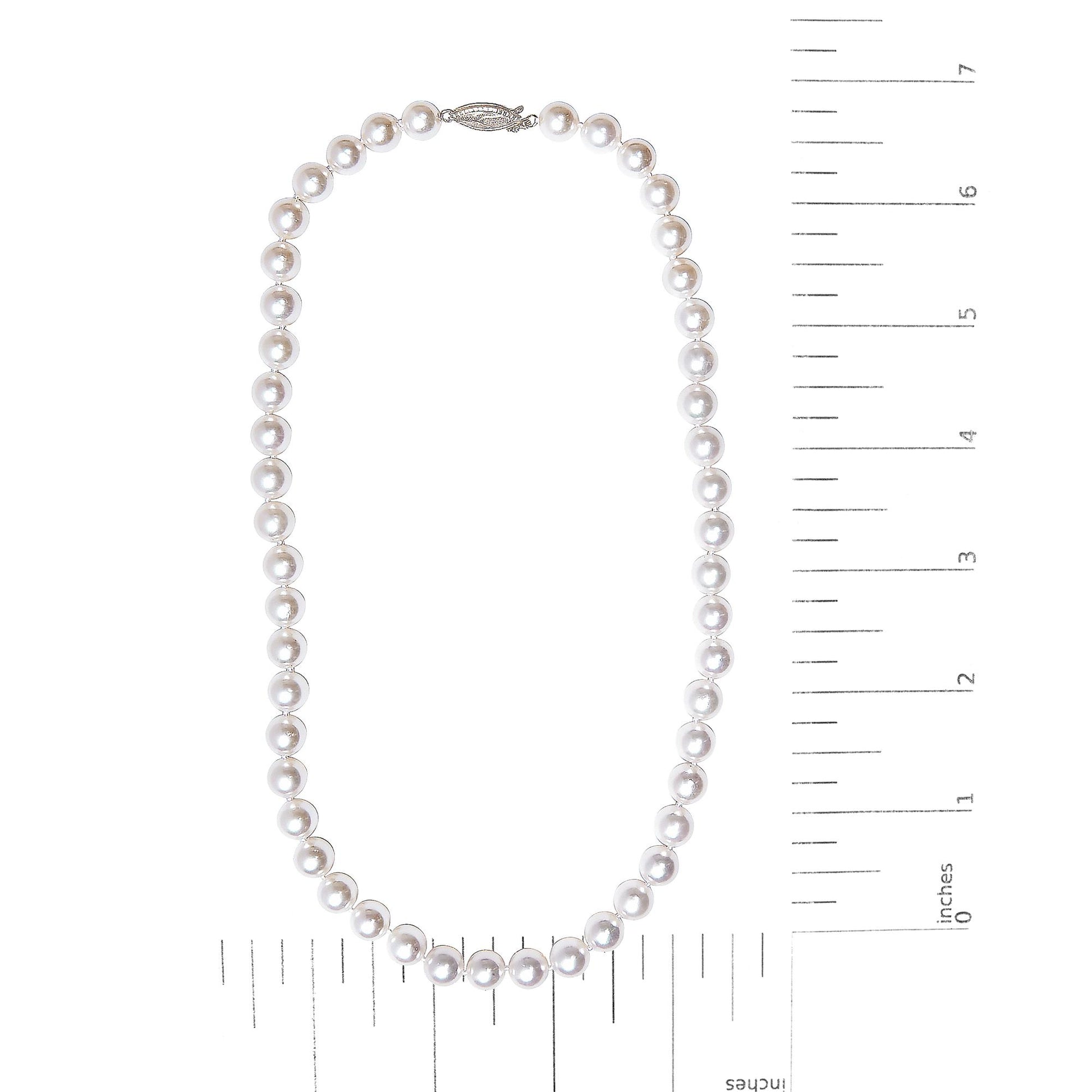 Top-down view of a white metal pearl necklace displayed flat on a measuring scale.
