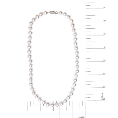 Top-down view of a white metal pearl necklace displayed flat on a measuring scale.
