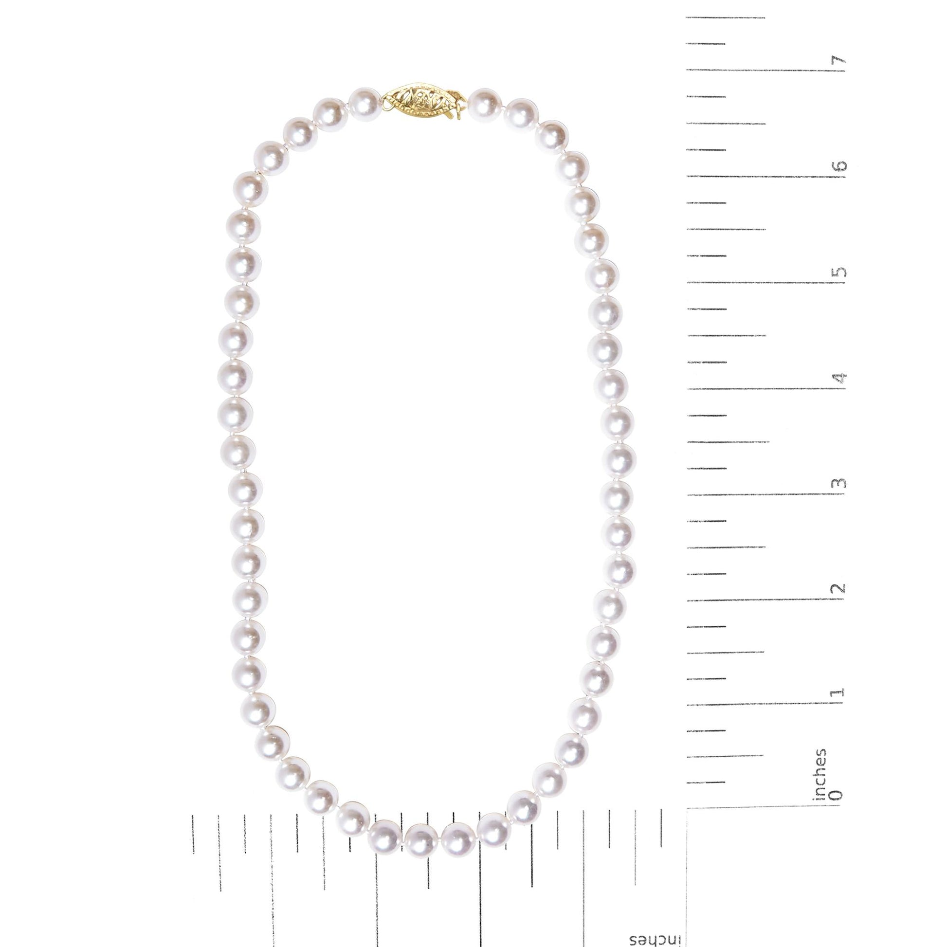 Top-down view of a necklace shown on a scale, featuring round white beads with a yellow metal clasp.