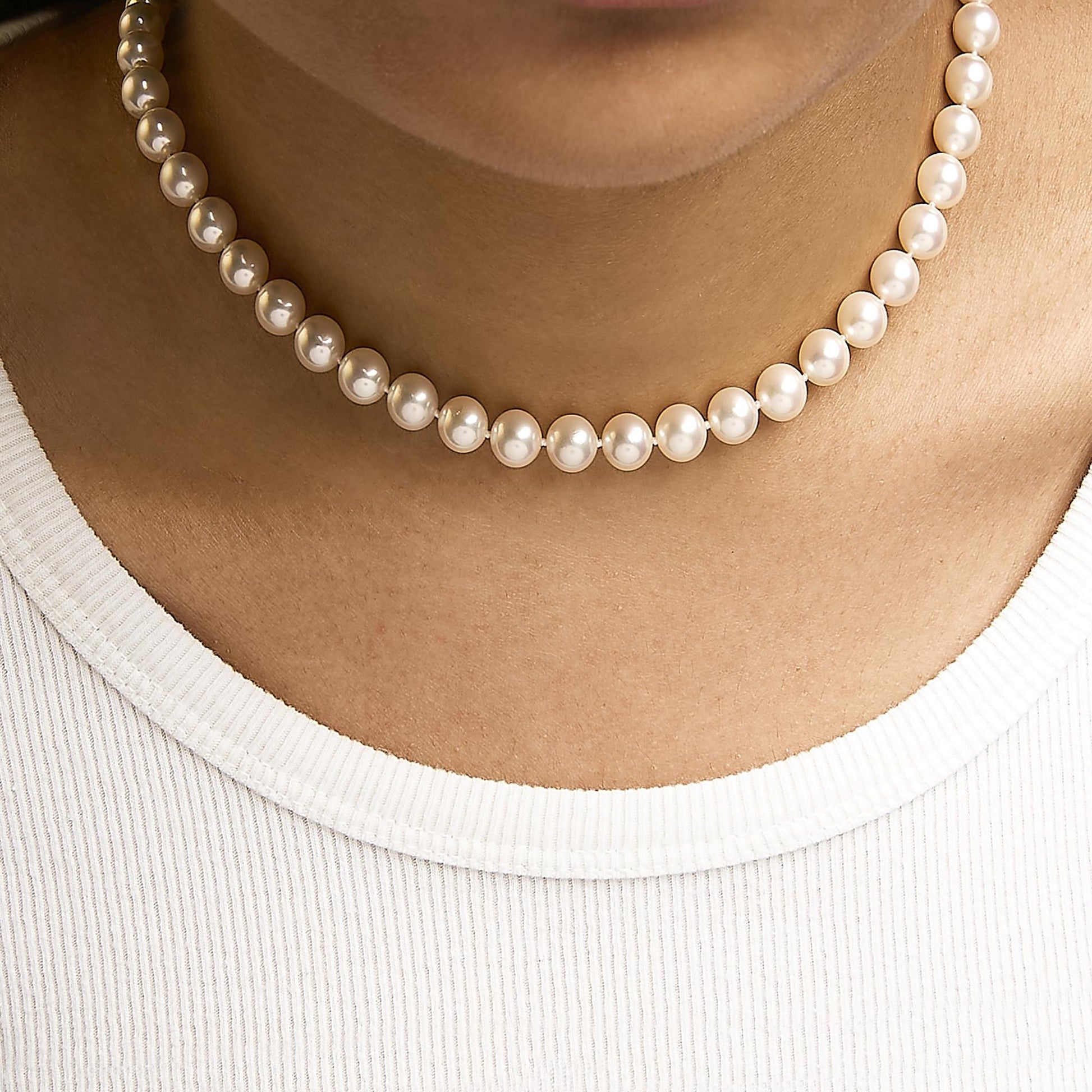 Close-up front view of a yellow metal necklace with round white gemstone beads, worn on a model's neck.