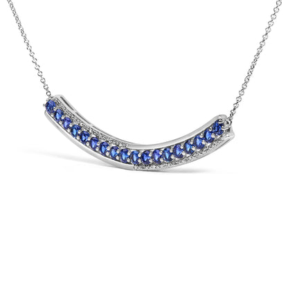 Close-up front angle of a curved white metal necklace pendant featuring prong-set round blue gemstones bordered by prong-set round white gemstones, shown on a white background.