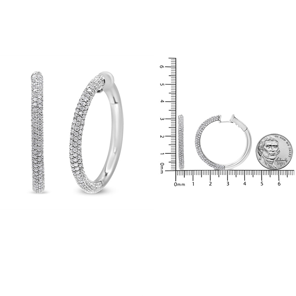 Pair of white metal hoop earrings paved with round white gemstones, shown from side and angled front views; also shown on a ruler and next to a coin for size reference.