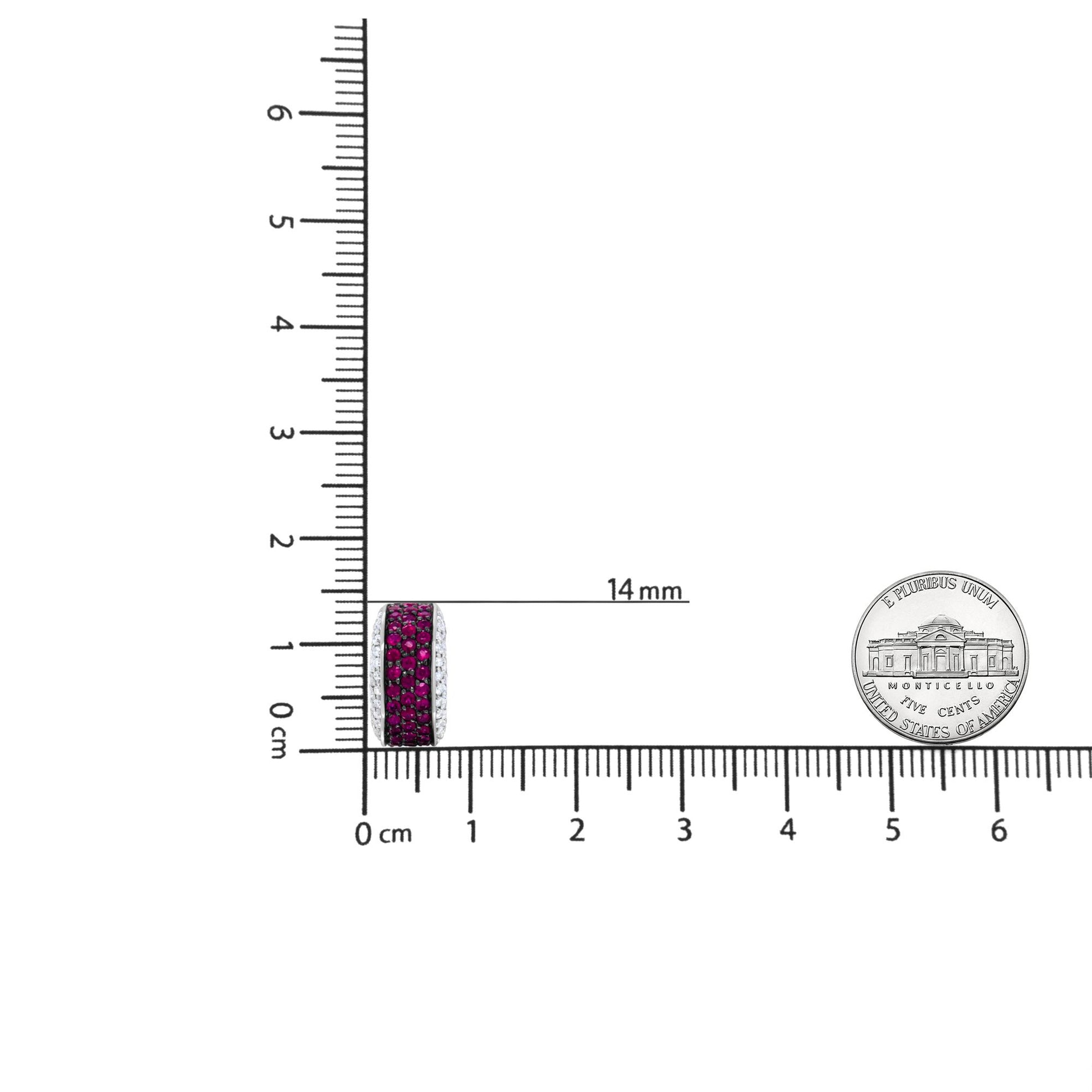 Close-up front view of white metal round hoop earring with rows of red and white round gemstones in prong settings, shown on a ruler and next to a coin for size reference.