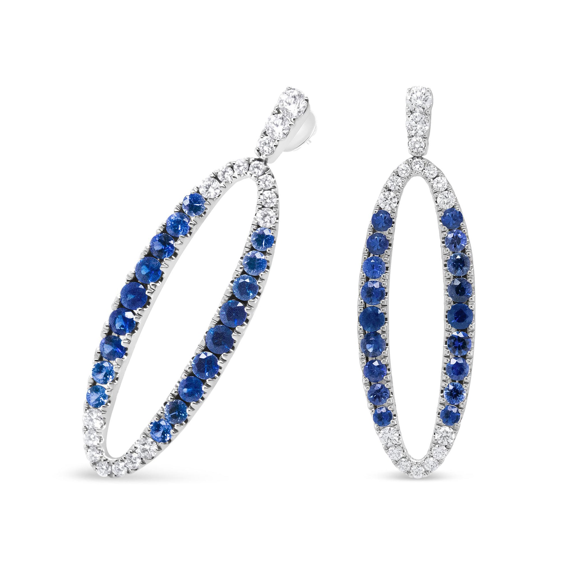 Pair of white metal oval-shaped earrings with alternating white and blue gemstones set in prong settings, shown from a front and side angle.