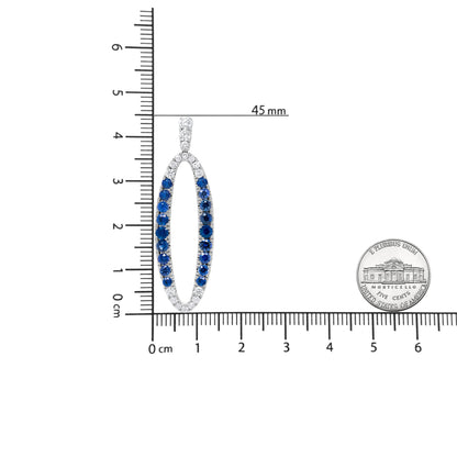 Oval white metal earring with alternating rows of white and blue gemstones, shown from the front on a ruler and with a coin for scale.