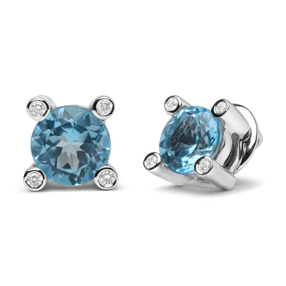 Pair of white metal stud earrings with round blue gemstones prong set at the center, surrounded by round white gemstones in bezel settings, front and angled side views on white background.