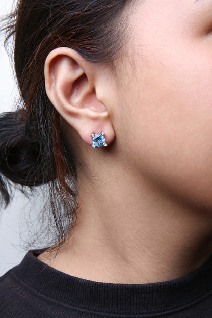 Close-up side view of a white metal stud earring on a model, featuring a round blue gemstone with four small round white gemstones around it.