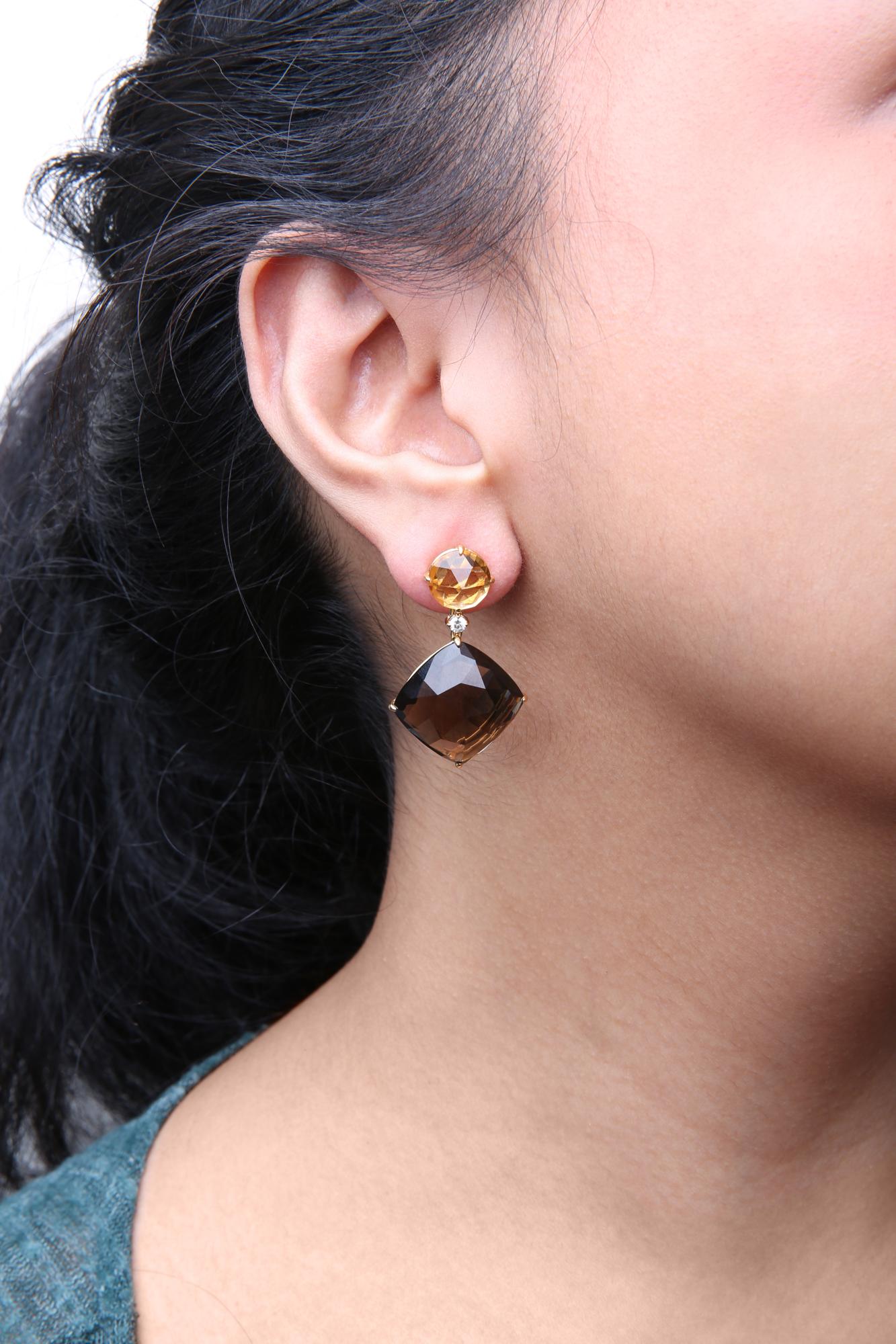 Close-up side view of a model wearing yellow metal earrings featuring a round yellow gemstone at the top, a small round white gemstone beneath it, and a cushion-shaped smoky gemstone dangling below.
