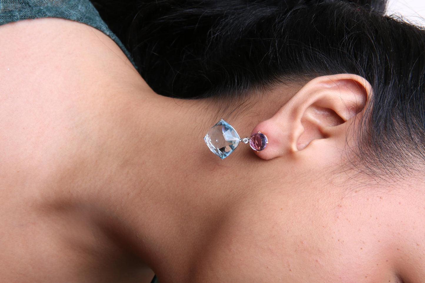 Yellow metal earrings with round white gemstone, black cushion-shaped gemstone, and round yellow gemstone in prong settings, worn on a model, side profile angle.