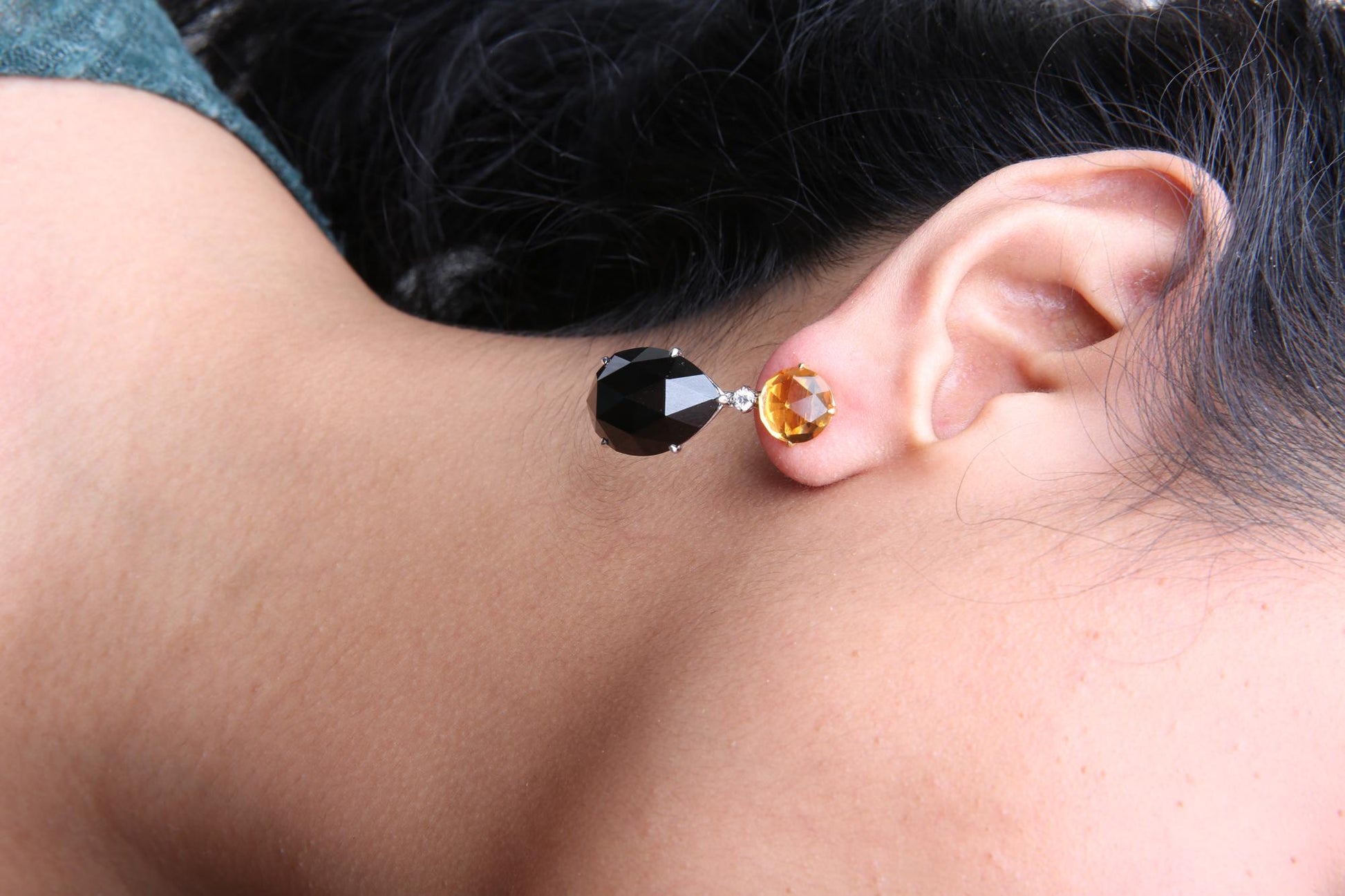 Close-up side view of a model wearing drop earrings featuring a yellow round gemstone at the top, a small white round gemstone below it, and a larger black pear-shaped gemstone hanging at the bottom.