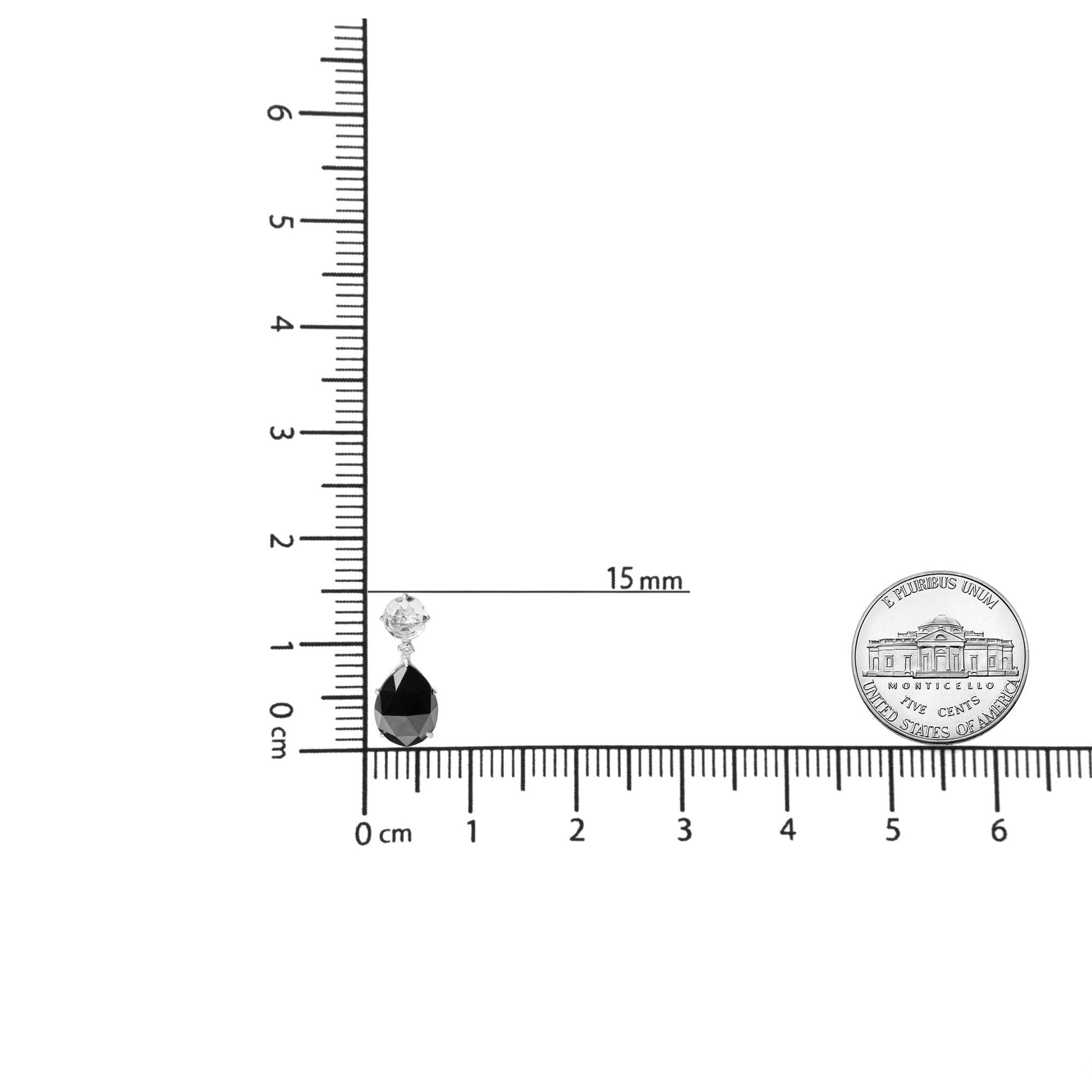 White metal earrings with a black pear-shaped gemstone and a white round gemstone above, shown on a ruler and scale for size reference, front-facing angle.
