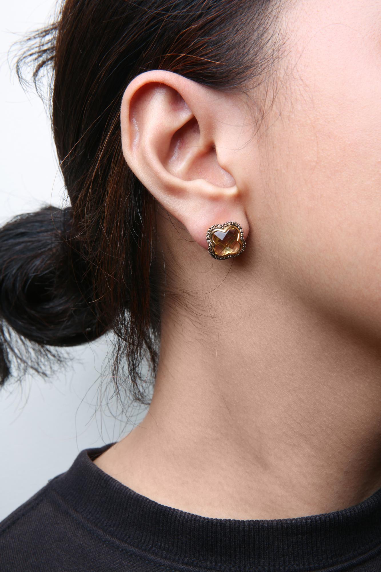 Close-up side view of a model wearing yellow and black earrings featuring a yellow gemstone with surrounding small brown round gemstones.