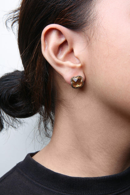 Close-up side view of a model wearing yellow and black earrings featuring a yellow gemstone with surrounding small brown round gemstones.