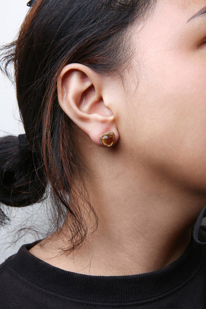 Close-up side view of a model wearing a yellow metal stud earring featuring a heart-shaped yellow gemstone surrounded by small round brown gemstones in prong settings.