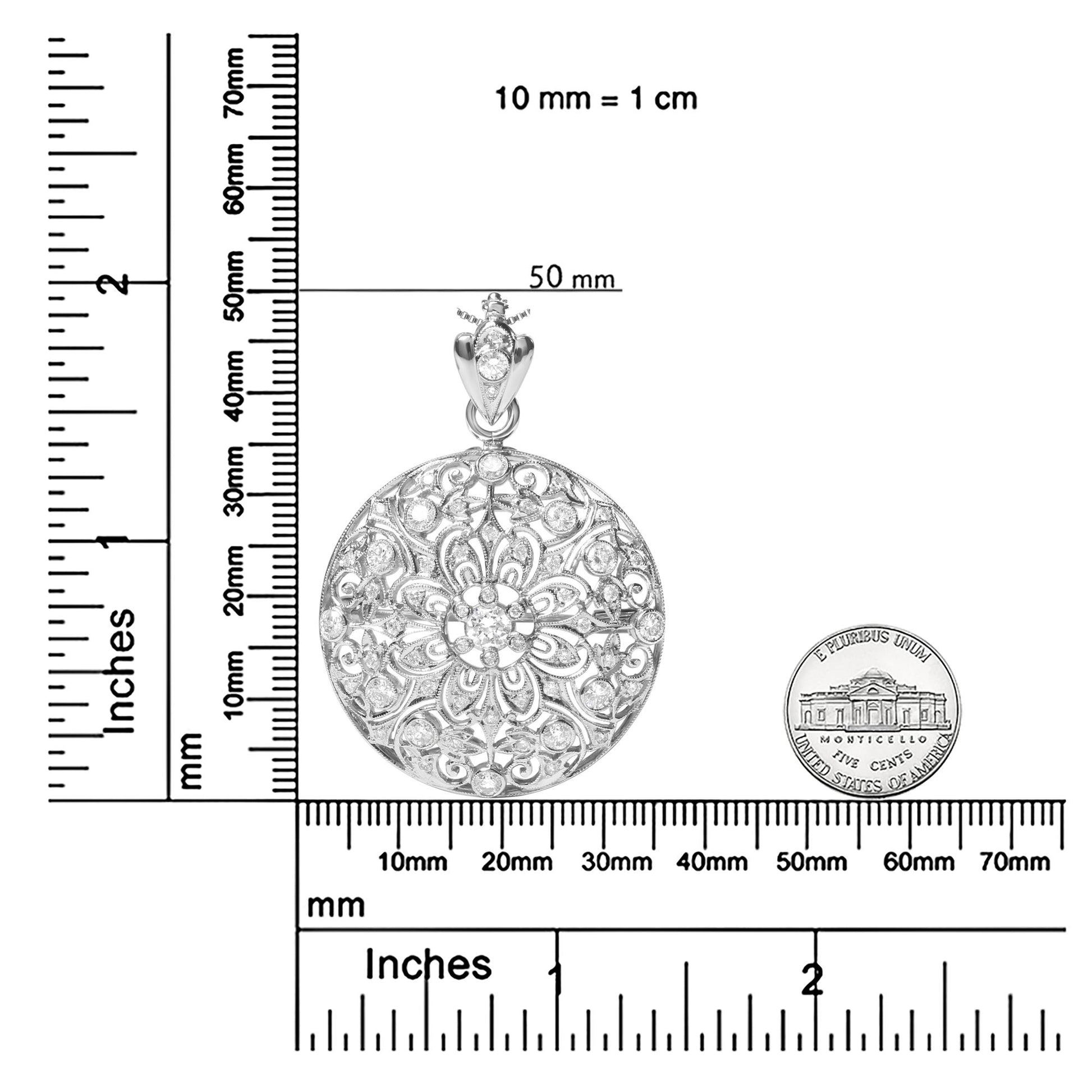 Top-down view of a round white metal brooch with intricate filigree and bezel-set white round gemstones, shown on rulers for size reference.