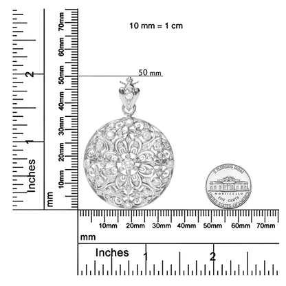 Top-down view of a round white metal brooch with intricate filigree and bezel-set white round gemstones, shown on rulers for size reference.