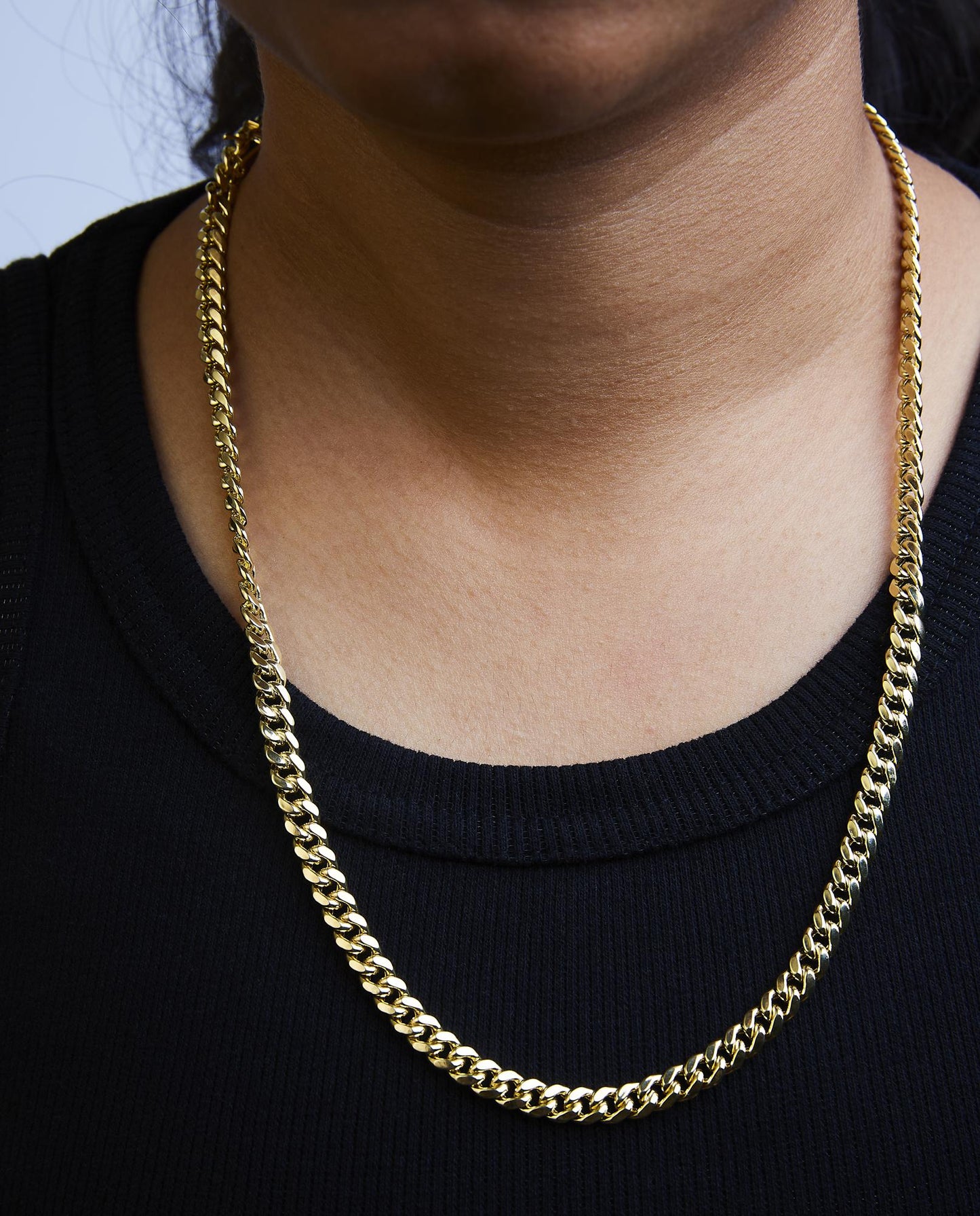 Close-up front view of a yellow metal chain necklace shown worn on a model against a black top.