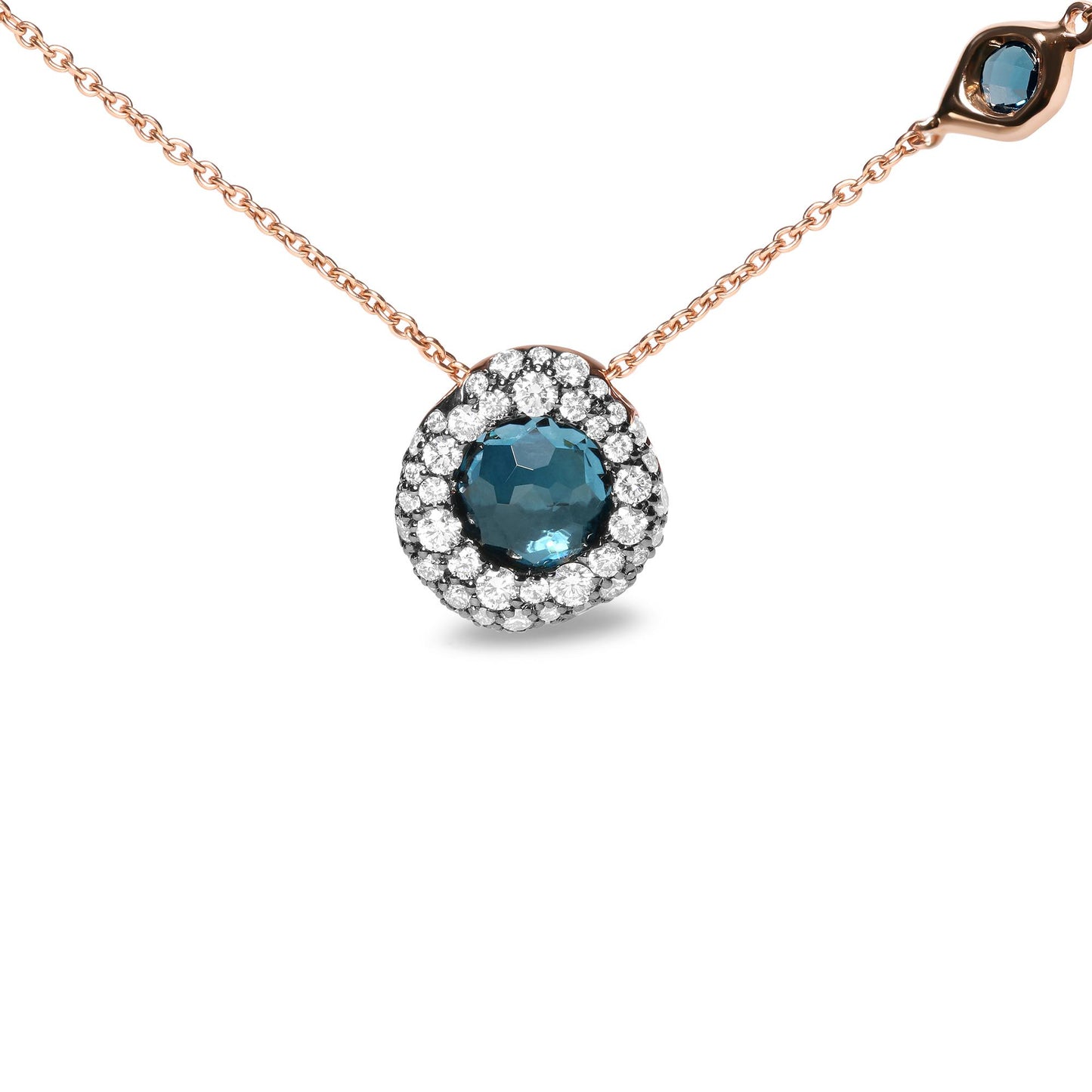 Close-up front angle of a rose metal necklace with a round blue gemstone pendant surrounded by small white gemstones in prong setting, featuring an additional small round blue gemstone and a small white gemstone in bezel settings on the chain.