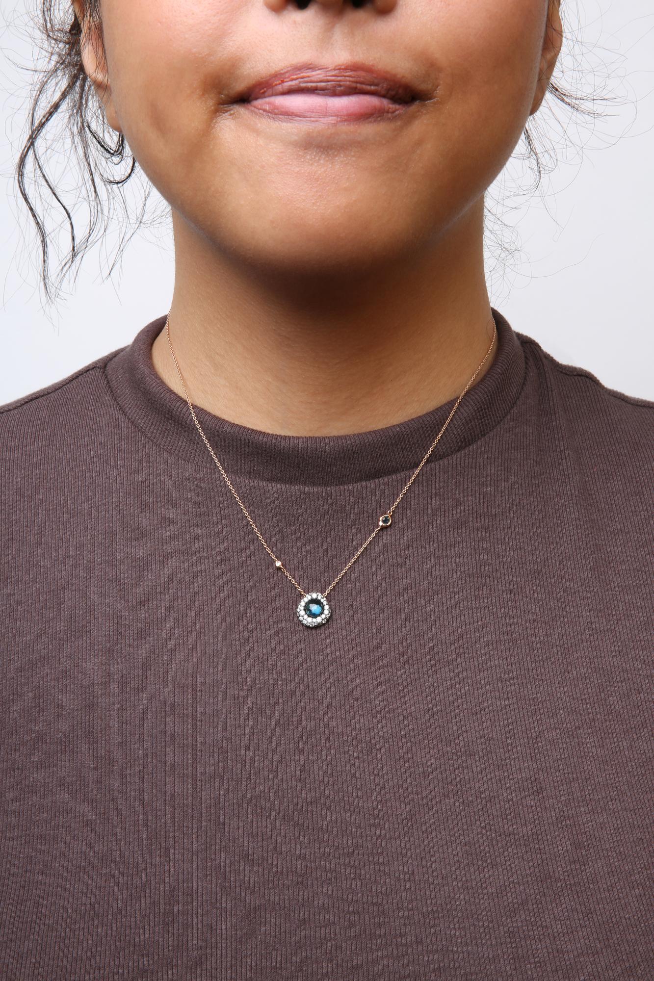Front view of a rose metal necklace with a round blue gemstone surrounded by white gemstones, worn on a model.