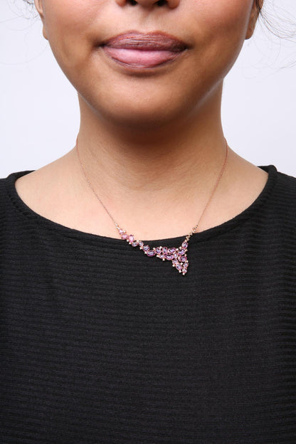 Close-up front view of a rose metal necklace on a model, featuring pink oval-shaped gemstones and brown round-shaped gemstones in prong settings, arranged in a V-shaped cluster.