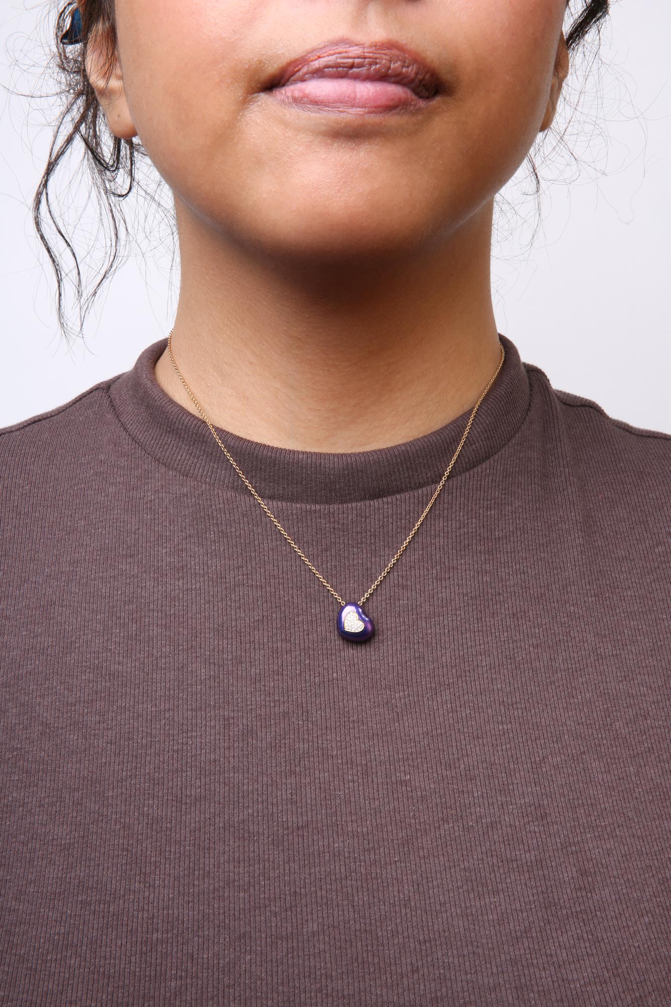 Close-up front view of a model wearing a yellow metal necklace with a purple heart-shaped pendant featuring a cluster of small white gemstones in a pave setting.