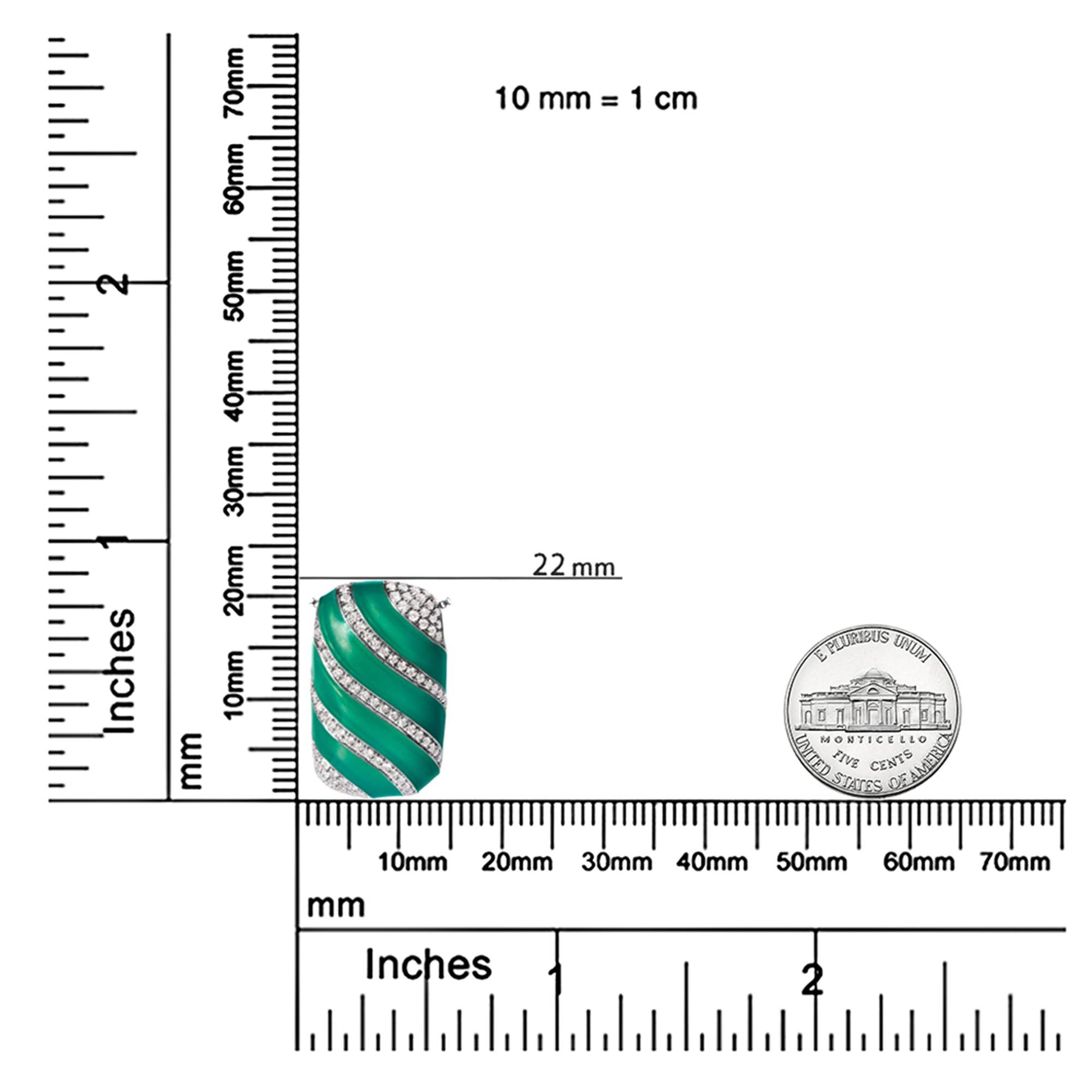 Close-up front angle of a white metal necklace pendant with green enamel diagonal stripes accented by rows of round white gemstones, shown on a ruler for size reference.