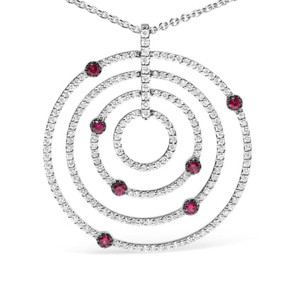 Front view of a white metal circular pendant necklace featuring multiple concentric circles adorned with small white gemstones and scattered red gemstones, shown against a white background.