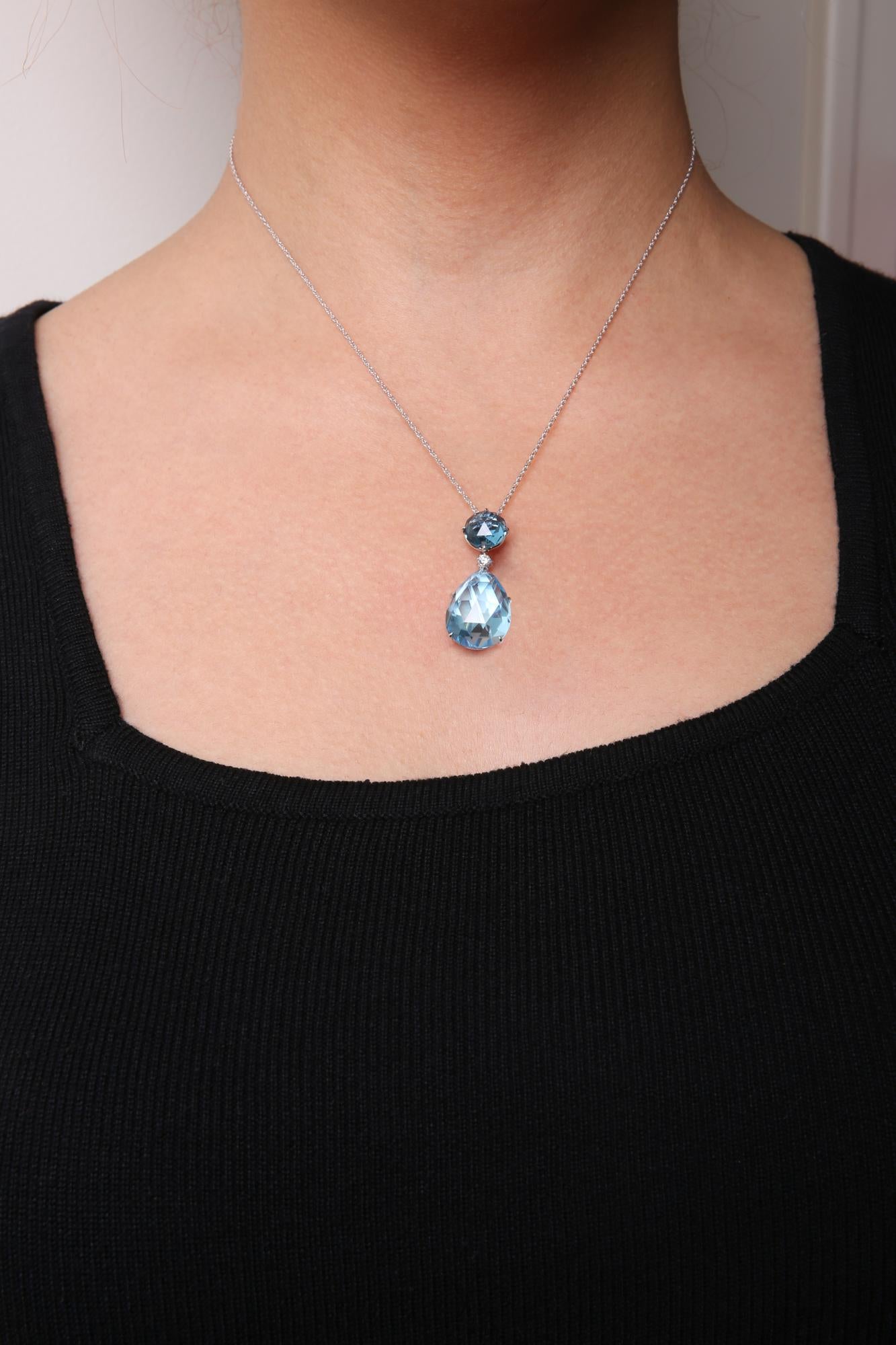 Close-up front view of a white metal necklace on a model, featuring one round white gemstone, one round blue gemstone, and one pear-shaped blue gemstone in prong settings.