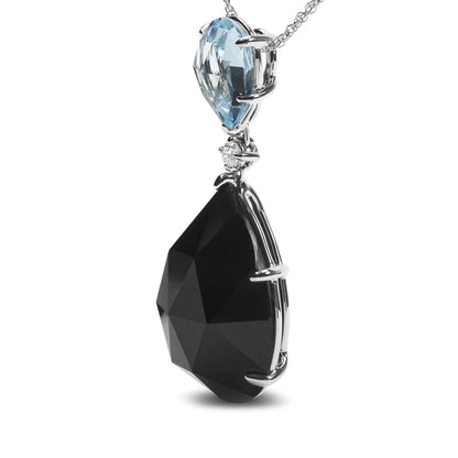 Close-up front view of a white metal necklace pendant featuring a prong-set blue pear-shaped gemstone on top, a small round white gemstone below it, and a larger prong-set black pear-shaped gemstone at the bottom.