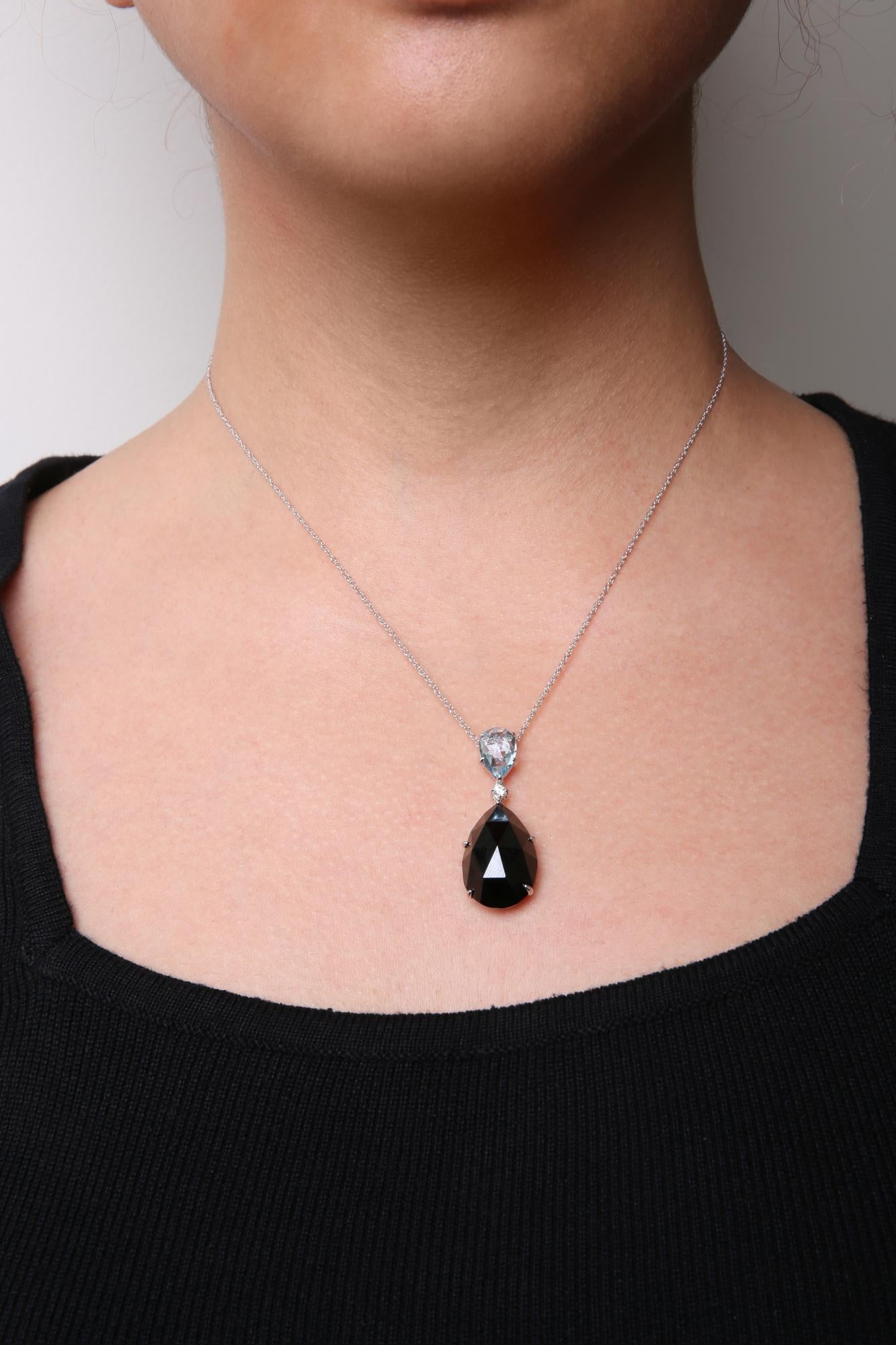 Front view of a white metal necklace on a model, featuring a pear-shaped black gemstone, a pear-shaped blue gemstone, and a round white gemstone in prong settings.