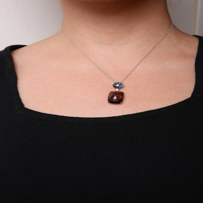 Front view of a necklace on a model featuring a white metal chain with a blue round gemstone, a small white round gemstone, and a smoky cushion-shaped gemstone pendant.