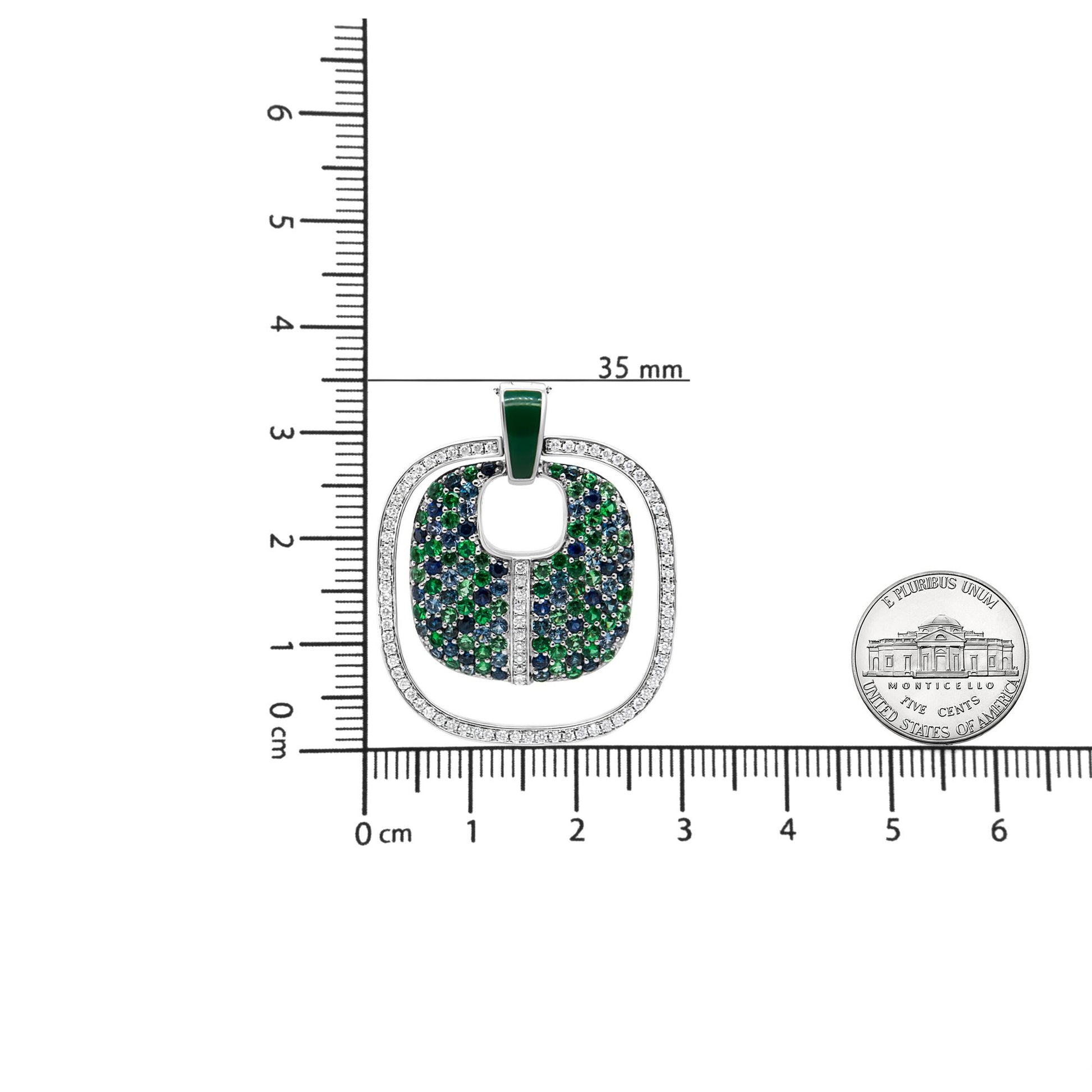 Top-down view of a white metal necklace pendant with an outer border of white round gemstones in prong settings, an inner area filled with blue and green gemstones, shown on a ruler with a coin for size reference.